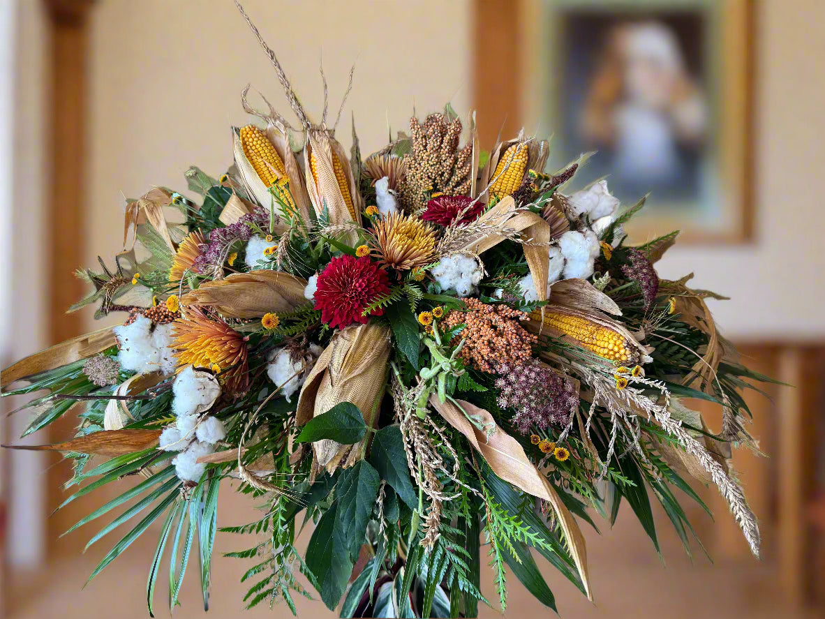 Casket Spray with Kansas crops and greenery against a wooden wall.