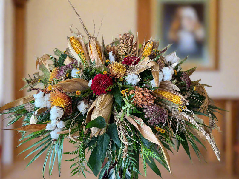 Casket Spray with Kansas crops and greenery against a wooden wall.